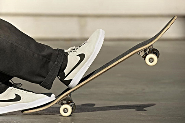 Người chơi mang giày thể thao trắng đạp đuôi skateboard để nâng mũi ván